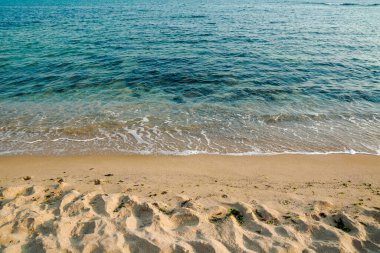 Denizde sakin bir sabah manzarası. Sabah vakti kumlu kumsal bomboş. Rahatlamak ve yaz tatili konsepti. Gökyüzünde bulutlar olan güneşli bir hava