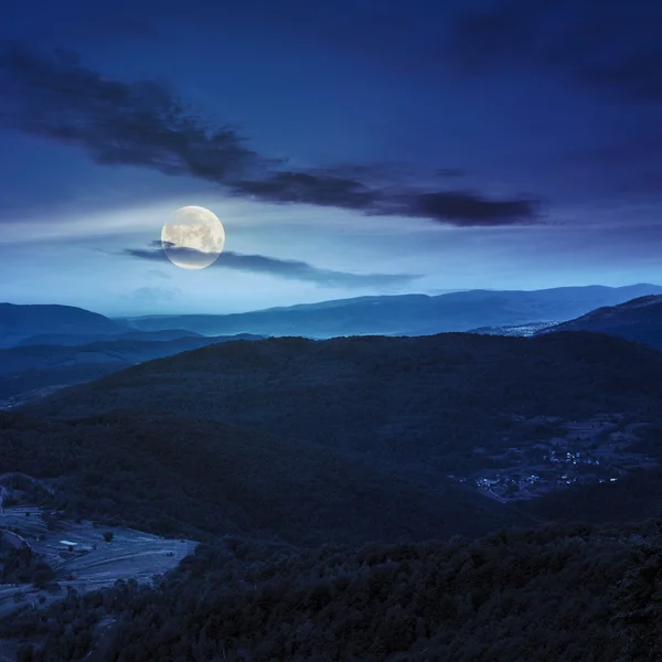 Aldeia no prado da encosta com floresta na montanha à noite — Fotografia de Stock