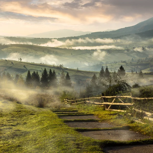 Steps down to village in foggy mountains at sunrise — Stock Photo, Image