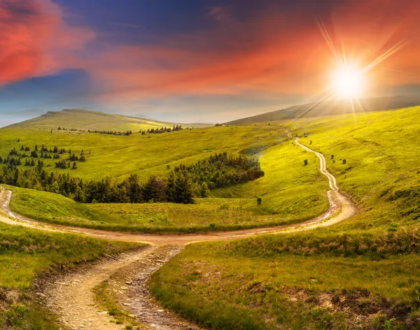 Cross road on hillside meadow in mountain at sunrise at sunset — Stock Photo, Image
