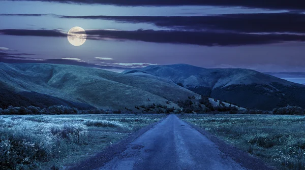 Nachts verlassene Straße durch Wiesen in Berg - Stockfotografie