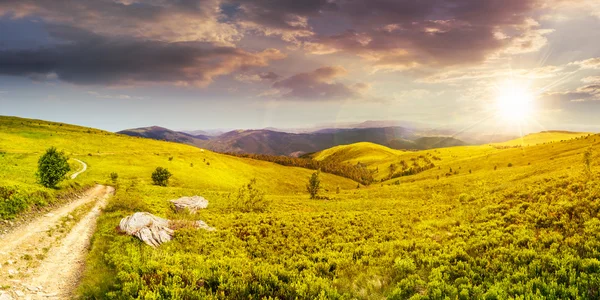 Estrada no prado de encosta no panorama da montanha ao pôr do sol — Fotografia de Stock