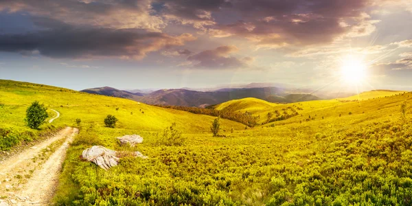 Strada su prato collinare in panorama montano al tramonto — Foto Stock