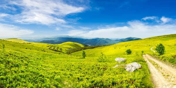 Road on hillside meadow in mountain panorama at sunrise — Stock Photo, Image