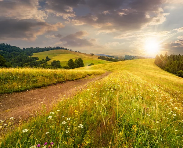 Estrada através do prado na encosta ao pôr do sol — Fotografia de Stock