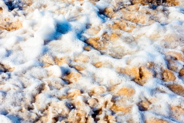 texture of sea foam on the sandy beach. scenic aqua splash. closeup natural abstract background on a sunny day. summer vacation season. frozen moment of salt water meets golden sand and make art mess
