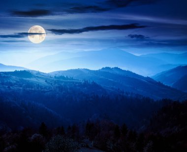 beautiful mountain landscape at night. wonderful countryside scenery in autumn season. rural pasture and trees on rolling hills in full moon light. hazy atmosphere