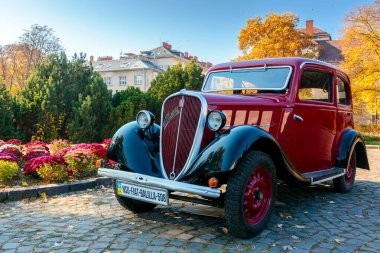 Uzhhorod, Ukrayna - 31 Ocak 2021: Izgarasında krom logosu olan kırmızı fiat 508 eski zamanlayıcı. Naroodna Meydanı 'ndaki sonbahar parkında güneşli bir hava. Sarı yapraklar ve çiçek tarlaları.