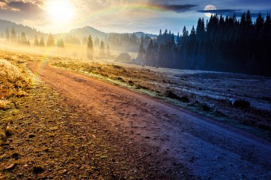 Sonbahar ekinoksunda dağ manzarası boyunca kırsal yol. Gündüz ve gece zaman kavramını değiştirir. Sis içinde yuvarlanan tepelerde kozalaklı orman. Güneş ve ay olan doğal park. güzel kırsal arkaplan