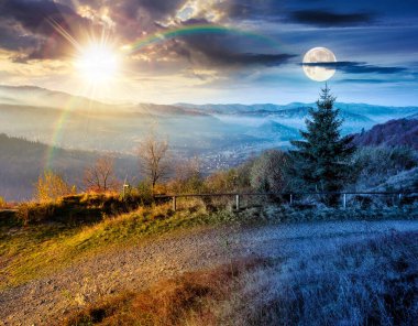 Dağdan sisli vadiye kadar bir manzara. Gündüz ve gece zaman kavramını değiştirir. Güzel sonbahar ekinoksu. Alacakaranlıkta güneşli ve aylı ormanlık tepeler. resimli dağlık kırsal alan manzarası