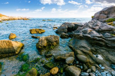 Mavi gökyüzünün altındaki kayalık deniz kıyısının güzel manzarası. Bulgaria sahilinin berrak sularıyla manzaralı bir yaz manzarası. Sahil tarafı geniş taşlarla kaplı, temiz bir Sozopol kasabası. Güneşli bir günde
