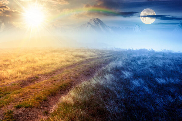 ландшафт с грунтовой дорогой через поле в тумане летом. концепция смены времени дня и ночи. Желтая трава на холмах под небом с солнцем и луной. таинственная атмосфера сельской местности композитное фото