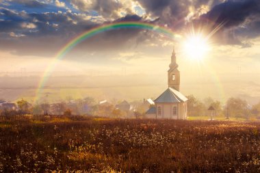 Sonbaharda gün batımında köyde eski bir kilise. Puslu bir akşam ışığında tepeden kırsal manzara. boş kırsal alanlar. Gökkuşağının altında hac hikayesi anlatımı