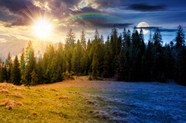 Bahar ekinoksunda ladin ormanları olan dağ manzarası. Gündüz ve gece zaman kavramını değiştirir. Tepedeki yeşil çayırda güneş ve ay var. Gökyüzünün altında bulutlarla kaplı uzak bir menzil. Güzel manzara.