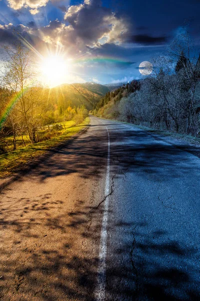 Sonbahar ekinoksunda dağ manzarası boyunca yol. Gündüz ve gece zaman kavramını değiştirir. Orman sonbahar renklerinde gökyüzü altında güneş ve ay ile. Uzakta karla kaplı zirve. manzaralı kırsal vadi