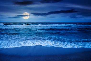Karadeniz dalgaları gece kumsala vuruyor. Dolunay ışığında karanlık bulutlu gökyüzünün altında rüzgarlı bir havada yaz tatili. Dramatik deniz manzarası. Yatırım veya soyut kavramlar için arkaplan