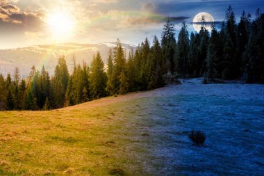 Bahar ekinoksunda ladin ormanları olan dağ manzarası. Gündüz ve gece zaman kavramını değiştirir. Tepedeki yeşil çayırda güneş ve ay var. Gökyüzünün altında bulutlarla kaplı uzak bir menzil. Güzel manzara.