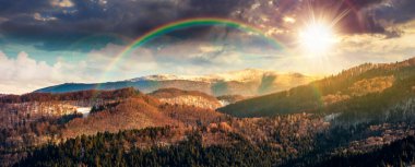 Gün batımında karlı tepeli uzak dağ sırtı manzarası. Akşam ışığında kırsal kesimin güzel, ormanlık bir tepesi. gökkuşağıyla kaplı sonsuz nostalji kitabı.