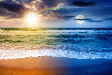 Deniz dalgaları kumsala çarpıyor. Gündüz ve gece zaman kavramını değiştirir. Yaz gündönümü rüzgarlı bir havada bulutlu gökyüzünün altında güneş ve ay ile. Dramatik deniz manzarası. ikilik ve geçiş şablonu
