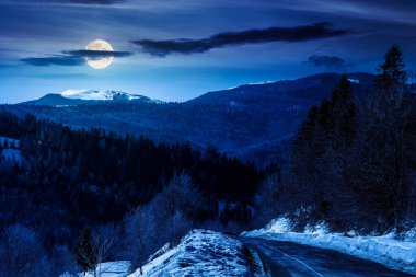 Geceleri karanlık gökyüzünün altında kışın dolambaçlı bir yol. Dolunay ışığında dağlar. Geçiş izni ve karla kaplı yamaçlarla seyahat. Yatırım finansmanı veya soyut kavramlar