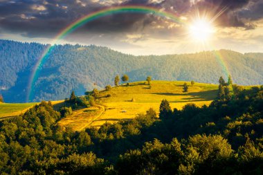Yaz günbatımında yuvarlanan tepelerle dağlık kırsal alan. Kırsal alanda akşam ışığında. Yeşil otlakları olan güzel bir yer. Gökkuşağının altında hikaye anlatımı sinemasal görüntü