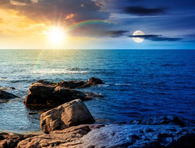 Deniz kıyısının kayalık kıyıları mavi gökyüzünün altında. Gündüz ve gece zaman kavramını değiştirir. Güneşin ve ayın altında güzel bir manzara. Tatil sezonunda tatil yeri manzarası. Uyum ve ilerleme takvimi