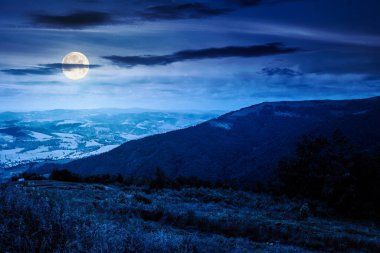 Geceleri bulutlarla dolu gökyüzü altında dağ manzarası. Çayır manzarası, dolunay ışığında yuvarlanan tepeler ve vadi. Yazın yürüyüş yeri. Yatırım veya soyut kavramlar için arkaplan