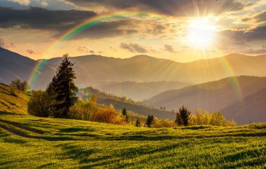 İlkbaharda gün batımında güzel bir kır manzarası. Akşam ışığında dağlık kırsal alanda yeşil çimenli yamaçlar. Tepeler uzaklığa doğru yuvarlanıyor. gökkuşağıyla kaplı sonsuz nostalji kitabı.