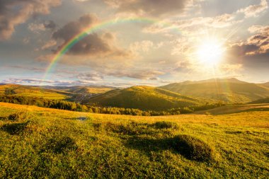 Gün batımında güzel bir kırsal bölge. Yazın harika manzarası akşam ışığında dağlarda. Çimenli tarlaların ve yuvarlanan tepelerin manzarası. Gökkuşağının altındaki kırsal manzara anlatımı görüntüsü