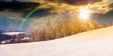 Gün batımında güzel bir kış manzarasının manzarası. Orman, akşam ışığında karla kaplı bir çayırda. Buz gibi havada donmakta olan ağaçlar. gökkuşağıyla kaplı sonsuz nostalji kitabı.