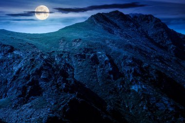 Yazın geceleri dağ manzarası. Mavi gökyüzünün altında dolunay ışığında bulutlar. Kayalık tepeleri ve dik yamaçları olan alp manzarası. Yatırım veya soyut kavramlar için yatay arkaplan