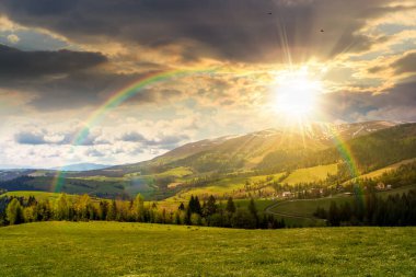 Baharda gün batımında dağlık kırsal alan. Akşam ışığında tepenin üstünde çimenli bir çayır. Tepeleri karla kaplı dağ sırtı. Gökyüzündeki bulutlar. umut, beklenti, yeni bir başlangıç ve parlak bir gelecek