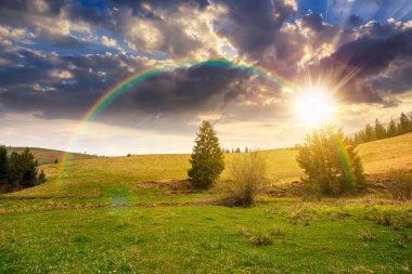 Baharda gün batımında bulutlu gökyüzünün altında yeşil tarlaları olan yuvarlanan bir tepe. manzaralı kırsal manzara dağları akşam ışığında. gökkuşağıyla kaplanmış sonsuz nostalji kitabı. Doğal güzellik estetiği