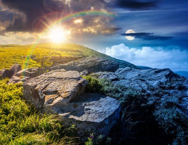 Yaz gündönümünde dağ manzarası. Gündüz ve gece zaman kavramını değiştirir. Tepenin yamacında yeşil çimenler ve kayalar, alacakaranlıkta güneş ve ay. Alp ortamında uzak bir yerin güzel manzarası