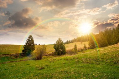 Baharda gün batımında bulutlu gökyüzünün altında yeşil tarlaları olan yuvarlanan bir tepe. manzaralı kırsal manzara dağları akşam ışığında. gökkuşağıyla kaplanmış sonsuz nostalji kitabı. Doğal güzellik estetiği