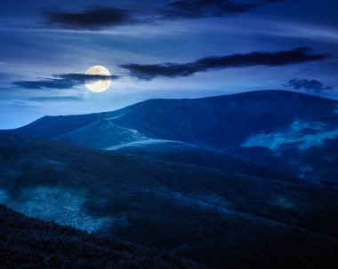 Yazın geceleri manzaralı dağ manzarası. Yuvarlanan tepelerle güzel bir seyahat geçmişi var. Dolunayda yemyeşil çimenli yamaçta benekli ışık. Dar bir telefon görüşü. gizemli fantezi