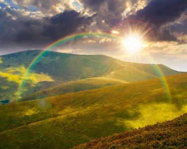 Yazın gün batımında manzaralı dağ manzarası. Yuvarlanan tepelerle güzel bir seyahat geçmişi var. Akşamları yemyeşil çimenli yamaçta benekli ışık. Dar bir telefon görüşü. Gökkuşağıyla hava
