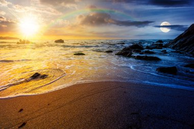 Denizde kumlu bir kumsal. Gündüz ve gece zaman kavramını değiştirir. Alacakaranlıkta güneş ve ay ile birlikte kayanın yanındaki kıyıya doğru yuvarlanan beyaz köpük. Mükemmel yaz tatili konsepti. Astroloji duvar kağıdı