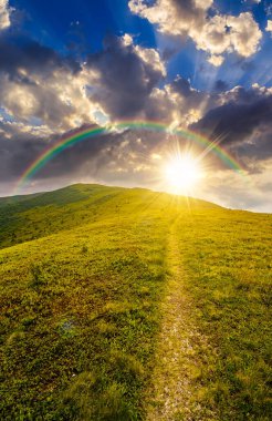 Gün batımında dağ manzarasında yürüyüş yapmak. Gökyüzünün altındaki dağ sıraları ve akşam ışığında bulutlar. Yeşil çimenli ve yuvarlanan tepeli manzara. gökkuşağıyla kaplı sonsuz nostalji kitabı.