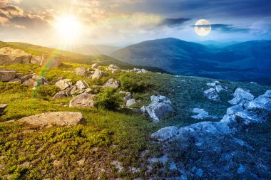 Yazın kayalarla kaplı dağ manzarası. Gündüz ve gece zaman kavramını değiştirir. Alacakaranlıkta güneş ve ay ile gökyüzünün altında çimenler. Alp çayırı ve kayalarla yuvarlanan tepeler. eşitlik ve kayma şablonu