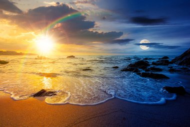 Denizde kumlu bir kumsal. Gündüz ve gece zaman kavramını değiştirir. Alacakaranlıkta güneş ve ay ile birlikte kayanın yanındaki kıyıya doğru yuvarlanan beyaz köpük. Mükemmel yaz tatili konsepti. Astroloji duvar kağıdı