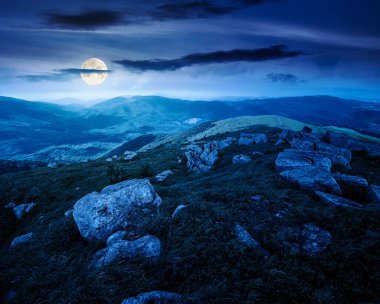 Yazın dağ manzarası ve geceleri kayalar. Dolunay ışığında karanlık gökyüzünün altında çimenler. Alp çayırı ve kayalarla yuvarlanan tepeler. Şeytani kurgu sanatı veya gizemli kavramlar için arkaplan