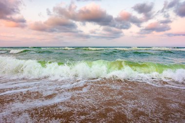 Kumlu sahilde fırtınalı bir hava var. Karadeniz üzerindeki dramatik gökyüzü. Sabah ışığında karamsar yaz manzarası. Sahile vuran yeşil dalgalar. Ufkun üzerindeki görkemli bulutlar