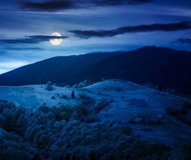 Geceleri kırsal dağ manzarası. Dolunay ışığında soğuk bir havada harika bir kır manzarası. Mayıs 'ta yuvarlanan tepelerin üstündeki bulutlu gökyüzü. kurgu sanatı veya gizem konsepti için arkaplan