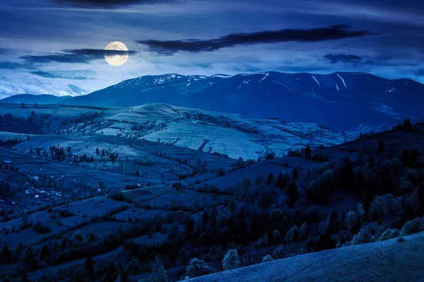 İlkbaharda geceleri kırsal alan. Dolunay, ormanlık tepelerle yuvarlanan kırsal manzaranın üzerinde. Vadinin güzel manzarası. Arka planda yüksek sıradağlar var. Açık hava fotoğrafçılığı için harika bir yer.