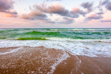 Kumlu sahilde fırtınalı bir hava var. Karadeniz üzerindeki dramatik gökyüzü. Sabah ışığında karamsar yaz manzarası. Sahile vuran yeşil dalgalar. Ufkun üzerindeki görkemli bulutlar