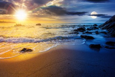 Denizde kumlu bir kumsal. Gündüz ve gece zaman kavramını değiştirir. Alacakaranlıkta güneş ve ay ile birlikte kayanın yanındaki kıyıya doğru yuvarlanan beyaz köpük. Mükemmel yaz tatili konsepti. Astroloji duvar kağıdı