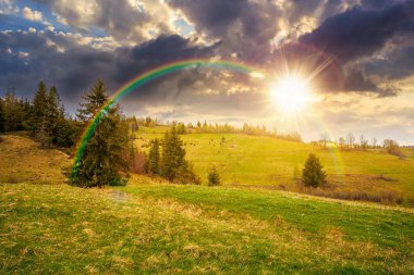 Baharda gün batımında bulutlu gökyüzünün altında yeşil tarlaları olan yuvarlanan bir tepe. manzaralı kırsal manzara dağları akşam ışığında. gökkuşağıyla kaplanmış sonsuz nostalji kitabı. Doğal güzellik estetiği