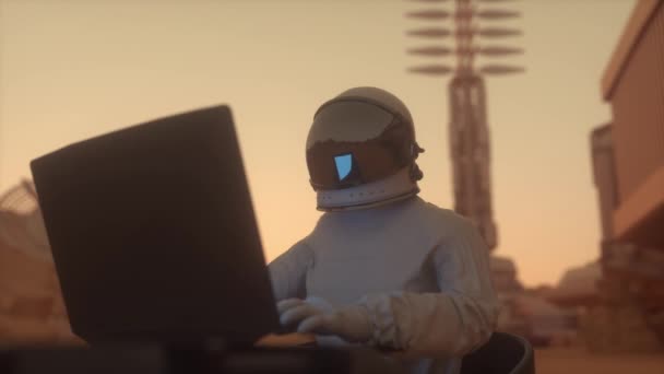 Астронавт в скафандре работает на ноутбуке в космической колонии на одной из планет. Марсианская колонизация — стоковое видео
