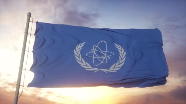 Bendera Badan Energi Atom Internasional IAEA melambaikan tangan dalam angin, langit dan latar belakang matahari — Stok Video